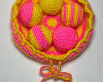May include: A handmade crochet set featuring a round basket and five balls. The basket and balls are in bright pink and yellow. The basket has a scalloped edge and a drawstring closure with a bow. The balls are either solid yellow or pink and yellow striped.
