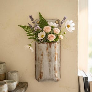 May include: A wall-mounted ceramic pocket vase with a glossy, mottled grey and brown glaze, secured by two brass screws. The vase is filled with a floral arrangement consisting of pink roses, white cosmos flowers, purple lavender sprigs, and green fern leaves.