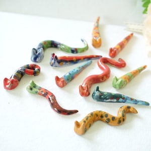 May include: A selection of brightly coloured ceramic worm figurines. Each worm is individually painted with a variety of colours, including red, blue, green, and yellow. The worms have a curved shape and are arranged on a white surface.