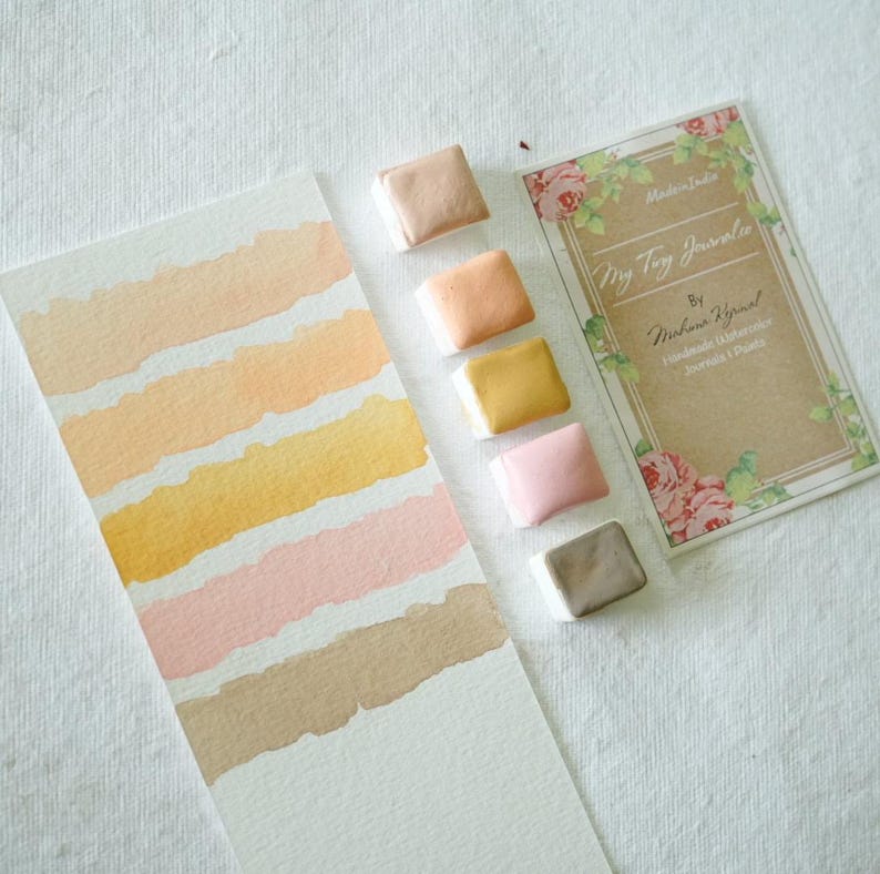 May include: Watercolor paint set with a range of warm colors, including peach, yellow, and pink. A watercolor swatch card displays the colors. The set includes a card with the text "My Tiny Journaler" and floral accents.