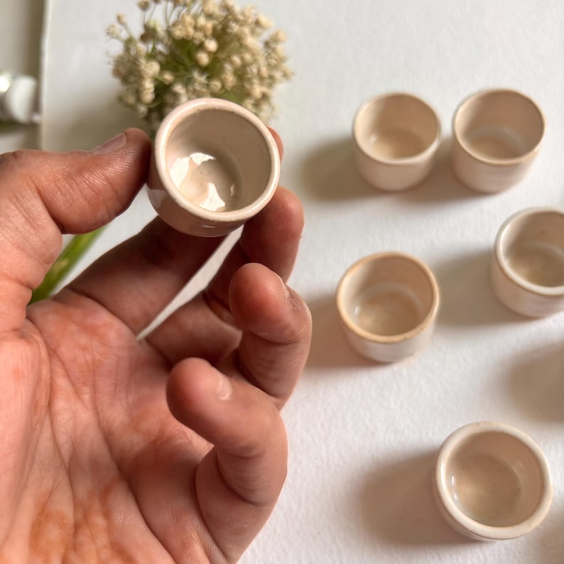 May include: Set of six small, white ceramic bowls. The bowls are round and have a smooth, glossy finish. They are perfect for serving small portions of food or for use as decorative accents.