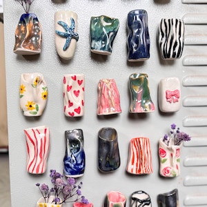 May include: A selection of small, colourful ceramic vases with distinctive designs. Some vases feature floral patterns, hearts, or abstract textures. Several vases hold dried flowers, adding a touch of natural beauty to the display.
