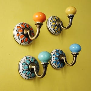 Peut inclure: Quatre patères murales décoratives avec des boutons en céramique colorés et des motifs floraux. Les boutons sont orange, jaune, turquoise et bleu. Les crochets ont une finition en laiton.