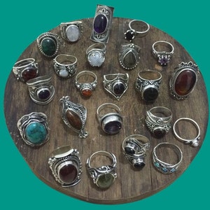 May include: A collection of silver rings with various gemstone inlays, including turquoise, amethyst, garnet, and agate. The rings are displayed on a wooden surface.