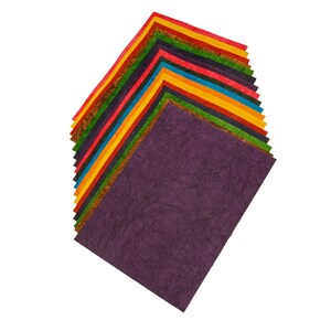 May include: A collection of colourful handmade paper sheets in shades of purple, orange, yellow, and green. The paper has a textured surface and is arranged diagonally against a white background.