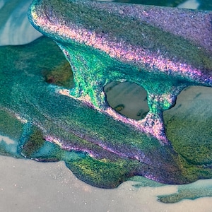 Può includere: Primo piano astratto di un'opera d'arte fluida con colori iridescenti. L'opera presenta strati fluidi di tonalità verde acqua, verdi e viola, creando un effetto scintillante. Il pezzo ha una finitura lucida e una forma organica unica.