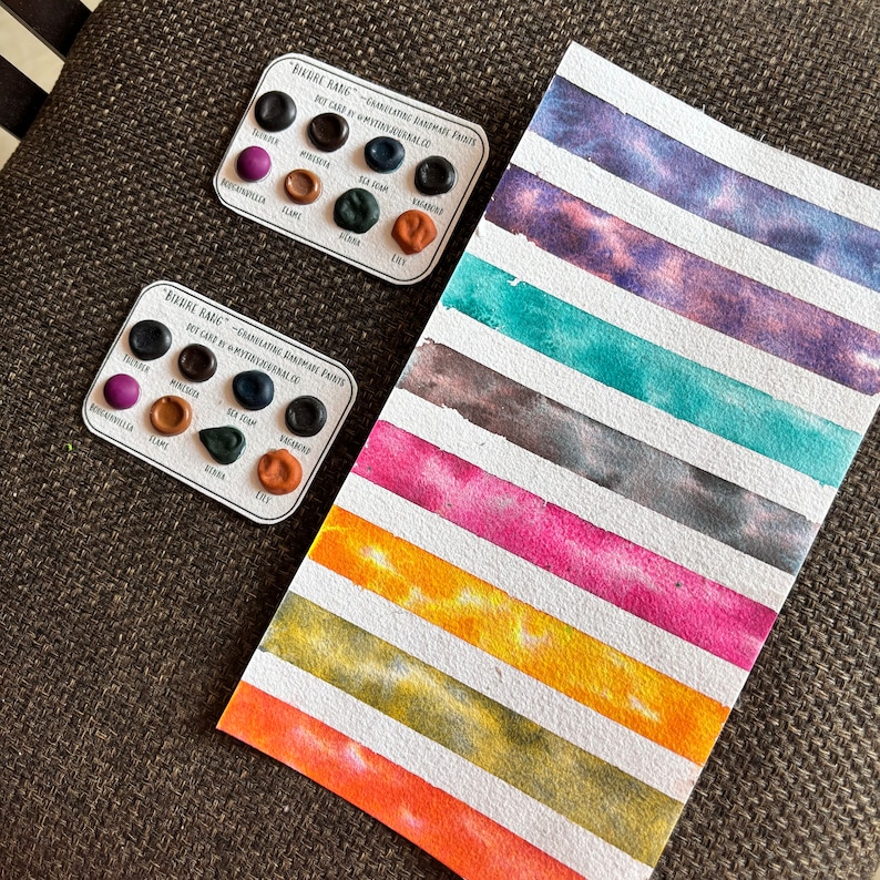 May include: Two dot card sets and a watercolor swatch card. The dot cards have various colors, with text that reads "PIERRE RANG - GRANULATING HANDMADE PAINTS". The swatch card has horizontal stripes of different colors, including pink, blue, and yellow.