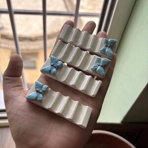 Puede incluir: Cuatro reposa palillos chinos de cer&aacute;mica blanca con un dise&ntilde;o acanalado. Cada reposa palillos presenta un adorno de lazo azul claro. Los reposa palillos est&aacute;n dise&ntilde;ados para sostener palillos chinos y son una adici&oacute;n decorativa a cualquier mesa.