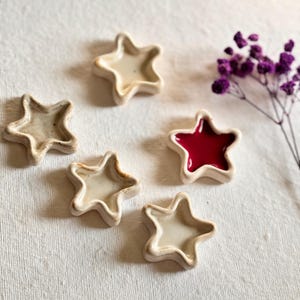 Puede incluir: Cinco platos de cerámica en forma de estrella de color blanco, cuatro están vacíos y uno contiene una pequeña cantidad de pintura roja.