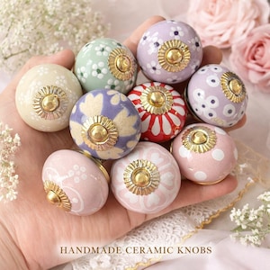 Può includere: Una collezione di pomelli in ceramica fatti a mano in vari colori e motivi. I pomelli presentano disegni floreali e a pois, con dettagli metallici color oro. La tavolozza dei colori comprende rosa, viola, verde e crema. Il testo "HANDMADE CERAMIC KNOBS" è visibile.