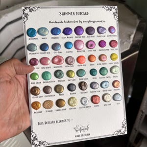 May include: A shimmer dotcard featuring handmade watercolors. The card displays a variety of colors, including blues, purples, pinks, greens, and golds. Text on the card reads "Shimmer Dotcard" and "Handmade Watercolors By @mytinyjournal.co."