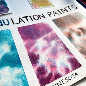May include: A close-up of watercolor paint swatches showing the color's texture and how it blends. The swatches are labeled "Minnesota" and "NULATiON PAiNTS".