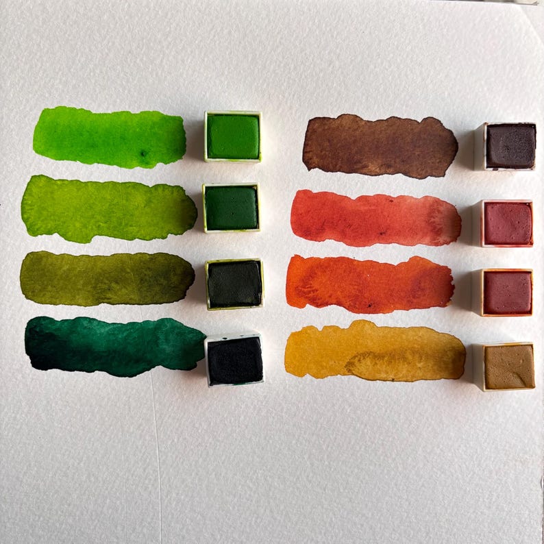 May include: Watercolor paint set with various shades of green, brown, red, and yellow. Each color is displayed as a swatch and in a small square pan. The swatches are painted on white paper.