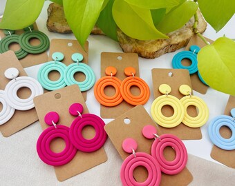 May include: Assortment of colorful, multi-layered, round earrings on brown card stock. The earrings are made of polymer clay and have a silver hook.