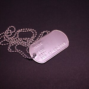 May include: A silver dog tag with a chain. The tag is engraved with the text "PONYO FISH HAM1 DOB 07-03-2009".