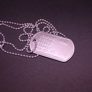 May include: A silver dog tag with a chain. The tag has the text "JENKINS, HOWL 6172005 HIZARD THIKLE DOB 01-27-1973" engraved on it.