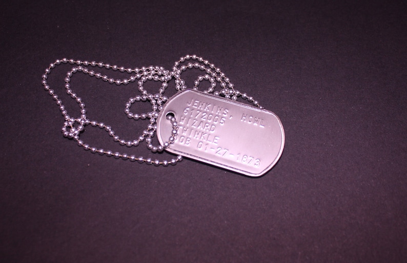 May include: A silver dog tag with a chain. The tag has the text "JENKINS, HOWL 6172005 HIZARD THIKLE DOB 01-27-1973" engraved on it.