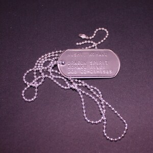 May include: A silver dog tag necklace with a silver chain. The dog tag has the text "RUSH, KONA KU DRAGON SPIRIT KOBAKU RIVER DOB 02-01-1989" engraved on it.