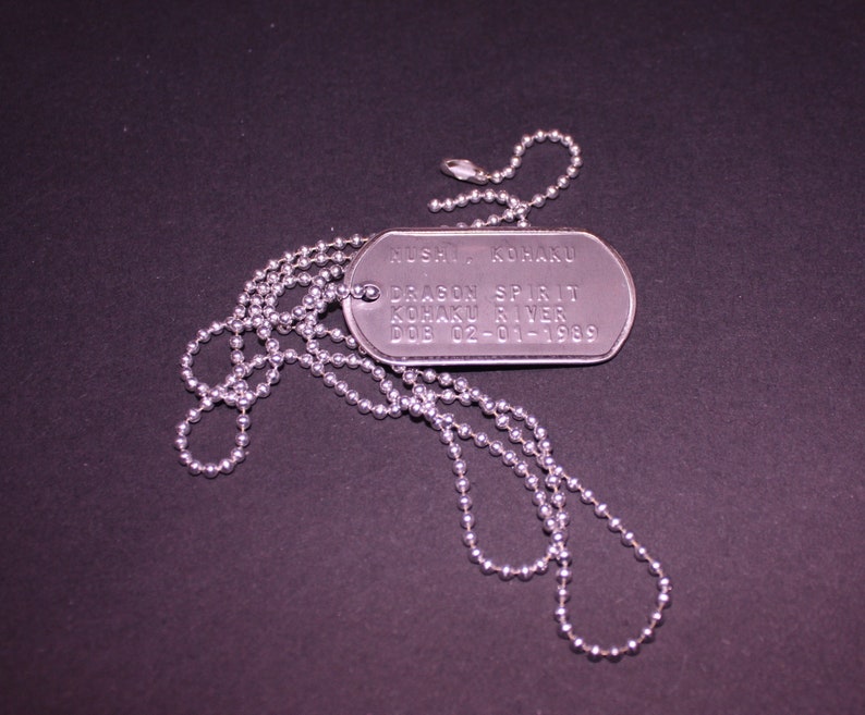 May include: A silver dog tag necklace with a silver chain. The dog tag has the text "RUSH, KONA KU DRAGON SPIRIT KOBAKU RIVER DOB 02-01-1989" engraved on it.