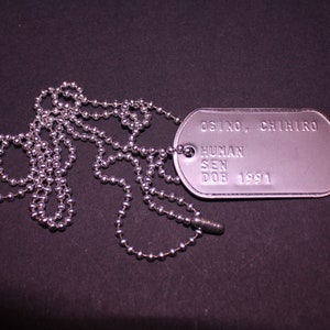 May include: A silver dog tag necklace with a silver chain. The dog tag has the text "OSINO, CHIHIRO HUMAN SEN DOB 1991" engraved on it.