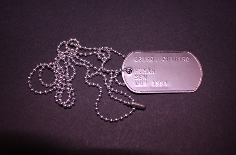 May include: A silver dog tag necklace with a silver chain. The dog tag has the text "OSINO, CHIHIRO HUMAN SEN DOB 1991" engraved on it.