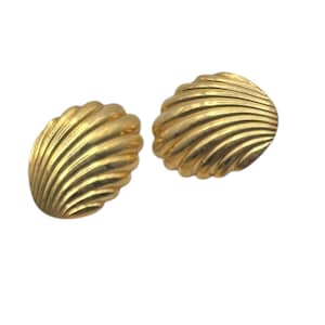 May include: Two gold-colored seashell-shaped earrings. Each earring has a ridged, fan-like design, and a rounded shape. The earrings are set against a white background.