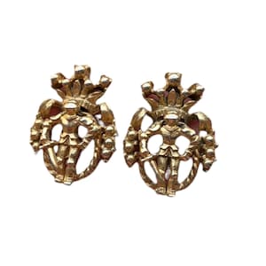 May include: A pair of gold-toned vintage earrings. Each earring features a detailed design of a figure within a decorative frame, topped with a crown. The earrings have a classic, ornate style, suitable for formal occasions.