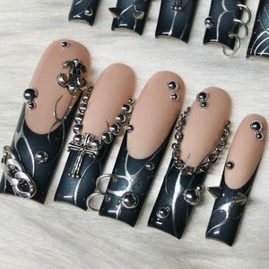 Puede incluir: Diez diseños de uñas en blanco y negro con detalles plateados y negros. Cada uña presenta un diseño diferente con cadenas plateadas, tachuelas y dijes. Los diseños incluyen cruces, cadenas y otros elementos de inspiración gótica.