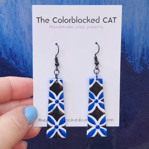 May include: A pair of blue and black clay earrings with a floral pattern. The earrings are on a white card with the text "The Colorblocked CAT Handmade clay jewelry thecolorblockedcat.com".
