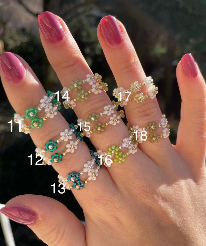 Puede incluir: Un conjunto de diez anillos de cuentas con dise&ntilde;os de flores en varios colores, incluyendo verde, blanco y azul. Los anillos est&aacute;n numerados del 11 al 18.