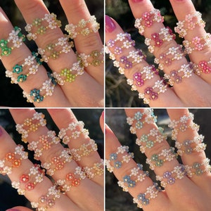 Puede incluir: Un conjunto de seis anillos de cuentas con dise&ntilde;os de flores en varios colores, incluyendo verde, rosa, blanco y azul. Los anillos est&aacute;n apilados en los dedos, mostrando los intrincados patrones florales.