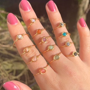 Op de afbeelding: Een handmodel draagt ​​een verscheidenheid aan gouden ringen met verschillende gekleurde stenen. De ringen zijn eenvoudig en delicaat, met een enkele steen in elke ring.