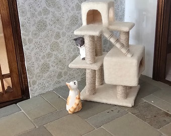 May include: A white cat tree with a beige base and a gray cat sitting on the top level. A smaller orange and white cat is sitting on the floor looking up at the cat tree.