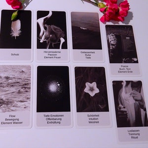 May include: A set of ten black and white tarot cards with German text. The cards depict images of a feather, fire, water, a flower, a book, a star, a flower, a hand holding a lighter, and a wave.