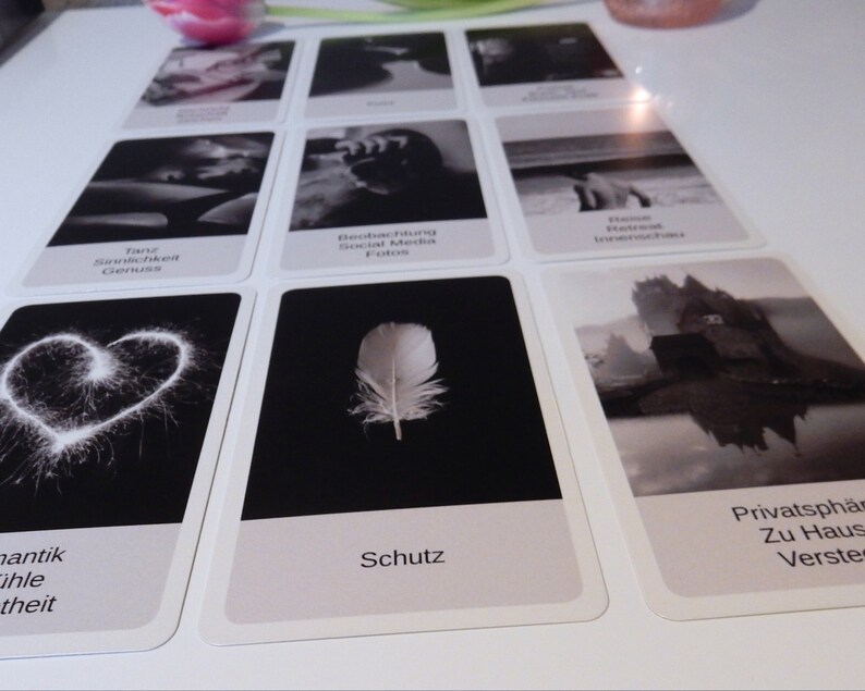 May include: Black and white oracle cards with images and text. The cards include images of a heart, a feather, a castle, and a person in water. The text on the cards includes words like "Taur Samlichk Genus", "Beobachtung Social Media Fotos", "Schutz", "Privatsph&auml; Zu Haus Verste", and "Romantik Ihle Theit".