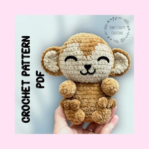 May include: Crochet pattern PDF for a brown and white plush monkey toy. The monkey has a smiling face with black eyes and a small black nose. The pattern is available for download.