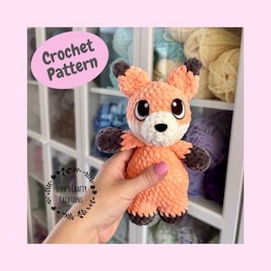 May include: A crocheted fox amigurumi toy with orange fur, black ears and feet, and white facial features. The toy is being held in a hand with pink nail polish.
