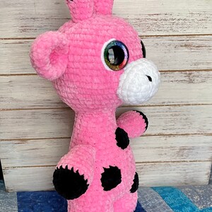 K&ouml;nnte beinhalten: Rosa geh&auml;keltes Giraffen-Pl&uuml;schtier mit schwarzen Flecken und gro&szlig;en glitzernden Augen.