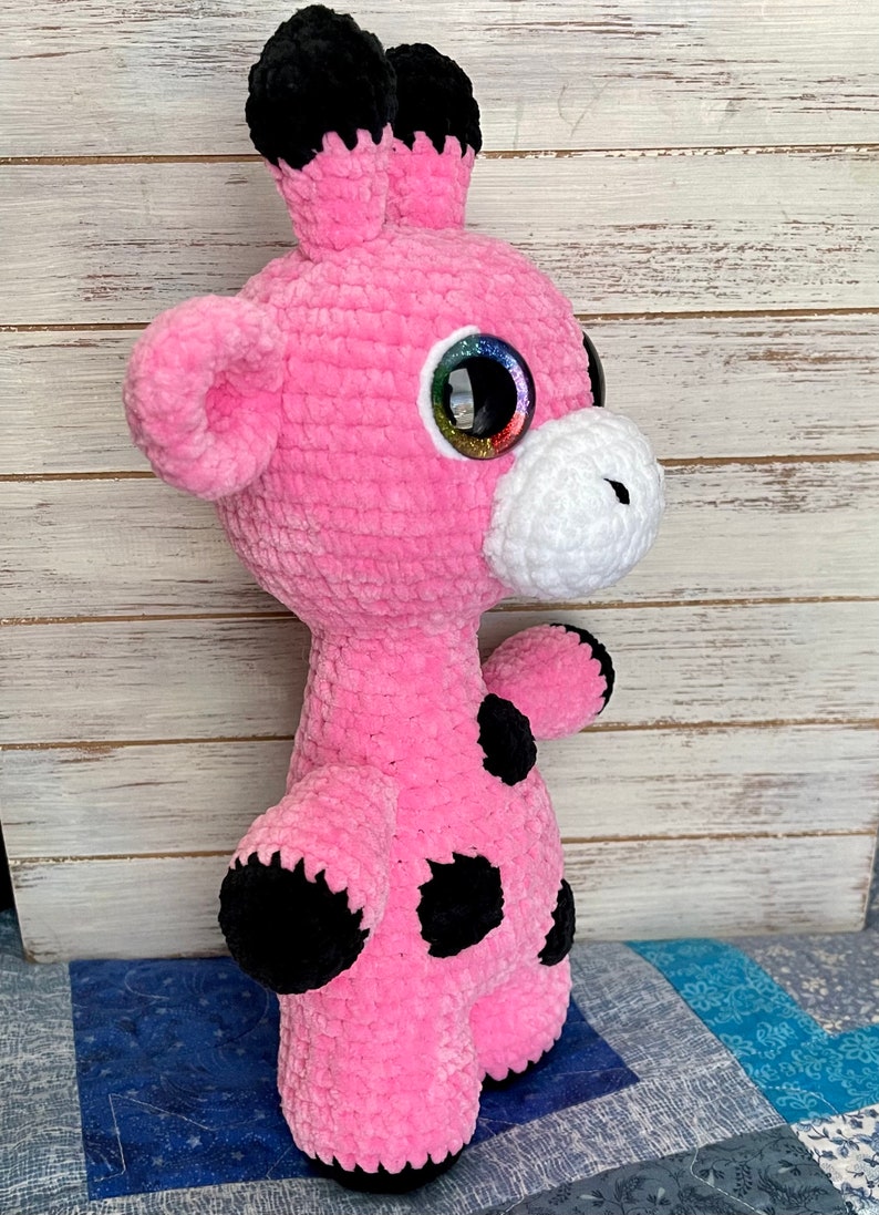 K&ouml;nnte beinhalten: Rosa geh&auml;keltes Giraffen-Pl&uuml;schtier mit schwarzen Flecken und gro&szlig;en glitzernden Augen.