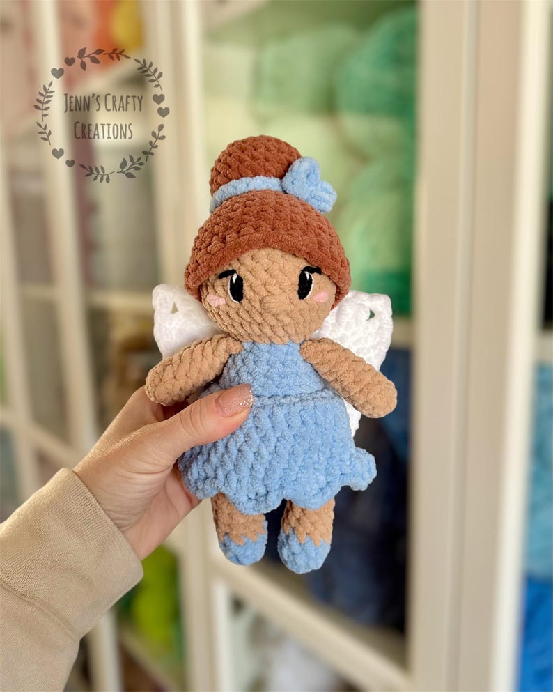 K&ouml;nnte beinhalten: Eine geh&auml;kelte Feenpuppe mit braunen Haaren, einem blauen Kleid und wei&szlig;en Fl&uuml;geln. Die Puppe h&auml;lt eine blaue Schleife in ihren Haaren.