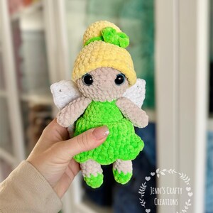 K&ouml;nnte beinhalten: Eine geh&auml;kelte Feenpuppe mit gelben Haaren, gr&uuml;nem Kleid und wei&szlig;en Fl&uuml;geln. Die Puppe h&auml;lt ein gr&uuml;nes Kleeblatt in ihren Haaren.