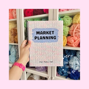 Può includere: Un quaderno a spirale con una copertina che recita "MARKET PLANNING" in testo nero su sfondo azzurro. La copertina presenta un motivo a maglia bianco e rosa. Il testo "Plan. Make. Sell." è sotto il titolo. Lo sfondo include scaffali di filati colorati.