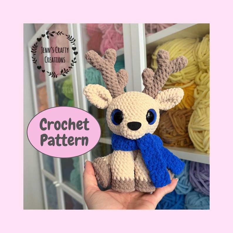 May include: A handmade crochet deer with a blue scarf, large blue eyes, and brown antlers. The deer is beige and brown, and the image includes the text "Crochet Pattern" and "Jenn's Crafty Creations."