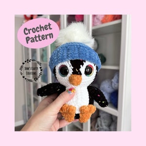 May include: A crocheted penguin toy with a blue hat and white pom-pom. The penguin has large, expressive eyes, an orange beak and feet, and black and white body. The image includes the text "Crochet Pattern" and "Jenn's Crafty Creations".