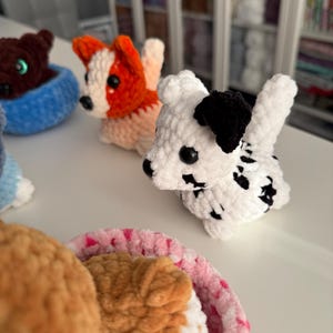 May include: Crocheted dog figurines in various colors, including white with black spots, orange and white, and brown. The dogs are in a basket and are handmade. The dogs are a cute and whimsical craft item.