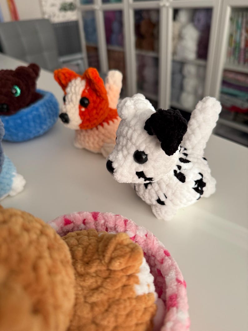 May include: Crocheted dog figurines in various colors, including white with black spots, orange and white, and brown. The dogs are in a basket and are handmade. The dogs are a cute and whimsical craft item.