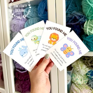 May include: Four white cards with the text "YOU FOUND ME" and cute animal illustrations: a whale, turtle, lion, and butterfly. Each card has a short message. The background shows shelves filled with colorful yarn.