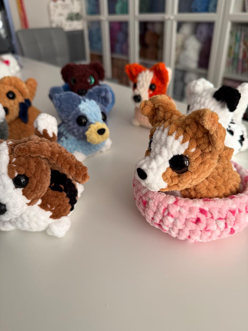 May include: A collection of handmade crochet dog toys in various colors and patterns. The dogs have black button eyes and are in different poses. One dog is in a pink bed.