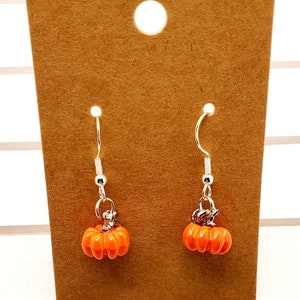 May include: A pair of silver pumpkin earrings with orange pumpkin charms. The earrings are on a brown card.