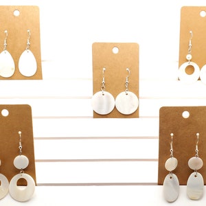 May include: Five pairs of white shell earrings on brown card stock. The earrings are all different styles, including round, oval, and circle shapes.